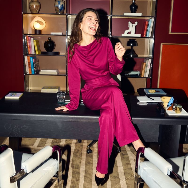 Model in a magenta two-piece outfit laughing on an office desk