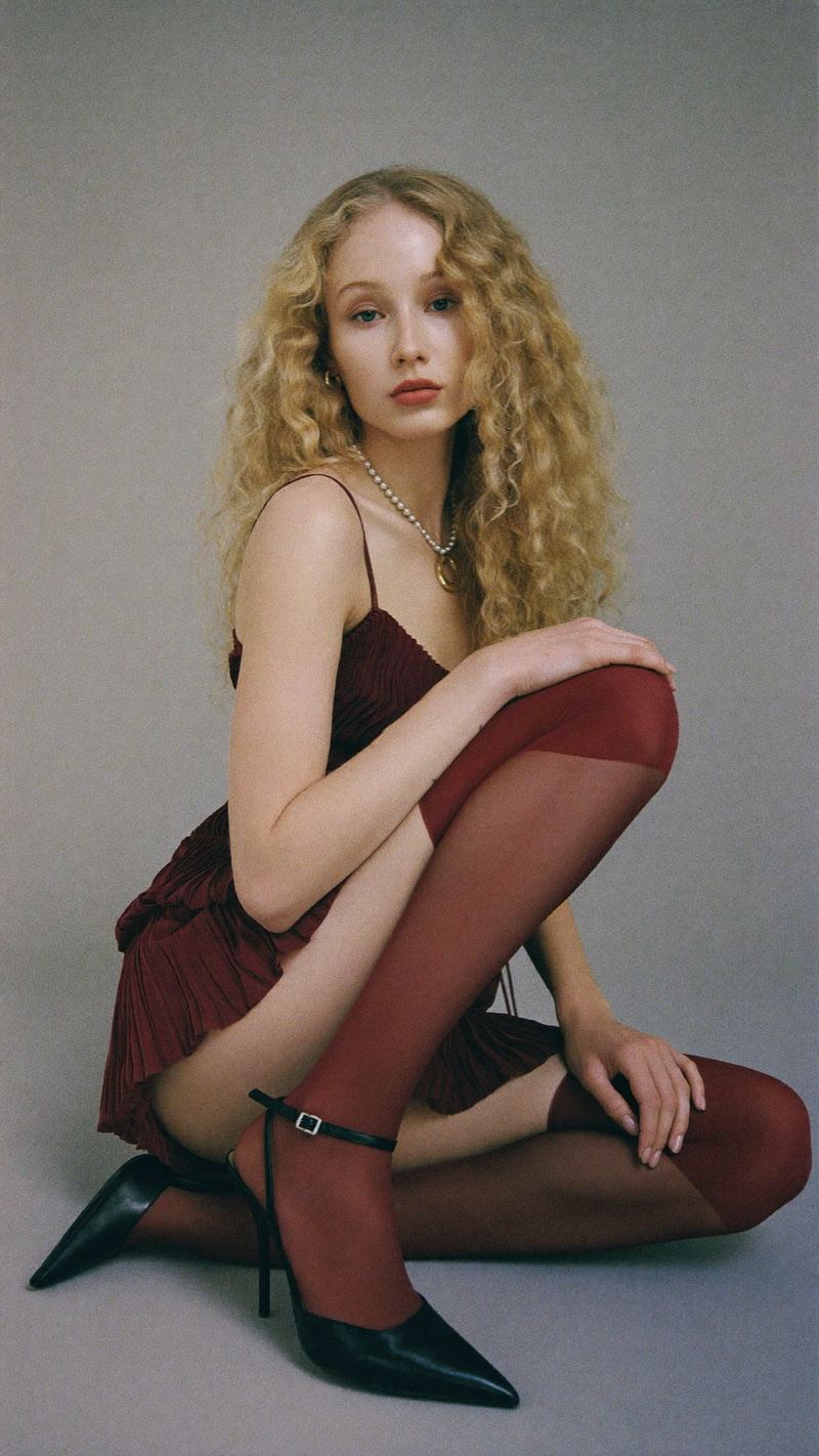 Editorial portrait in a burgundy pleated dress and stockings